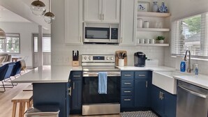 A modern kitchen with white cabinets, a stainless steel oven, and a microwave. There is a dining area with a wooden table and chairs. - Rock House - Lake Views & 15 Mins to Cedar Point (Huron)