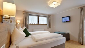 Una habitación de hotel moderna con una cama grande, un televisor de pantalla plana, una mesita de noche con lámpara y una ventana con cortinas.