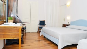 A hotel room with a wooden desk, a chair, a bed with a blue headboard, and a window with curtains. - B&B Casa D'Alleri Triple Room (Siracusa)