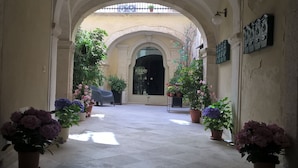 An arched corridor with potted plants, a bench, and a door labeled "ATELIER" in the distance. - B&B Casa D'Alleri Triple Room (Siracusa)