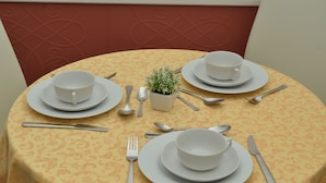 A round table with a yellow patterned tablecloth, set with white plates, bowls, cutlery, and a small potted plant. - B&B Casa D'Alleri Triple Room (Siracusa)