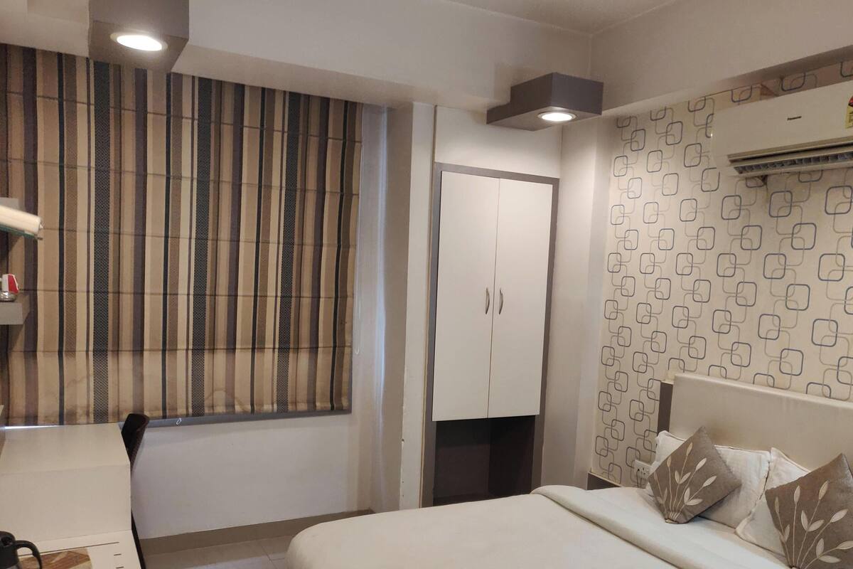 Habitació d'hotel amb un llit, un armari, una finestra amb cortines, un aparell d'aire condicionat i una paret amb un disseny.