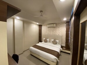 A modern hotel room with a large bed, a ceiling fan, and an air conditioning unit on the wall. - Starlit Select Nirvana (Varanasi)