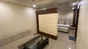 A modern living room with a sofa, a glass-top coffee table, and a decorative panel. - Starlit Select Nirvana (Varanasi)