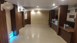 A spacious hotel lobby with a tiled floor, wooden paneling, a reception desk, and a standing fan. - Starlit Select Nirvana (Varanasi)