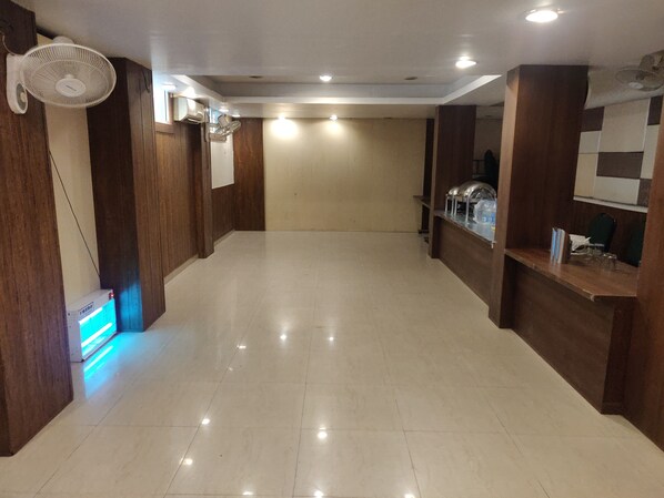 A spacious hotel lobby with a tiled floor, wooden paneling, a reception desk, and a standing fan. - Starlit Select Nirvana (Varanasi)