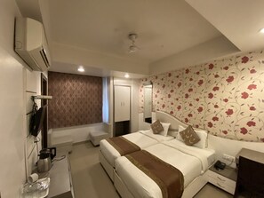 A hotel room with a large bed, a bedside table, a wardrobe, a mirror, and a patterned wall. - Starlit Select Nirvana (Varanasi)