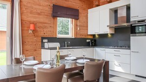 Une cuisine moderne avec des meubles blancs, un plan de travail noir et des appareils en acier inoxydable. On y trouve une table à manger avec des chaises et une bouteille de vin.