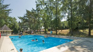 Une piscine entourée d’arbres, où des gens nagent et s’amusent.