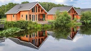 Deux cabanes en bois dotées de grandes fenêtres, avec un étang devant.