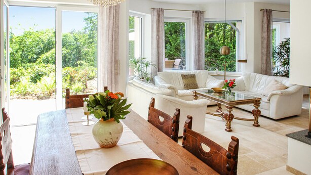A spacious living room with a white sofa, a wooden dining table, and a view of lush greenery through large windows. - Amazing home in Nideggen with WiFi (Nideggen)