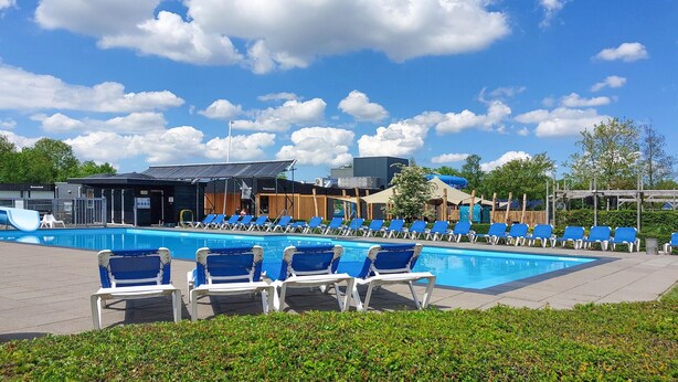 Una piscina con sillas azules, un área techada y un edificio con un letrero.