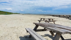 Una playa con una mesa de picnic de madera y un rompeolas rocoso.