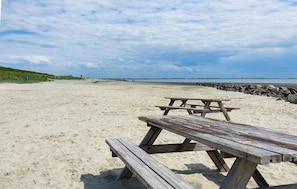 A beach with a wooden picnic table and a rocky breakwater.