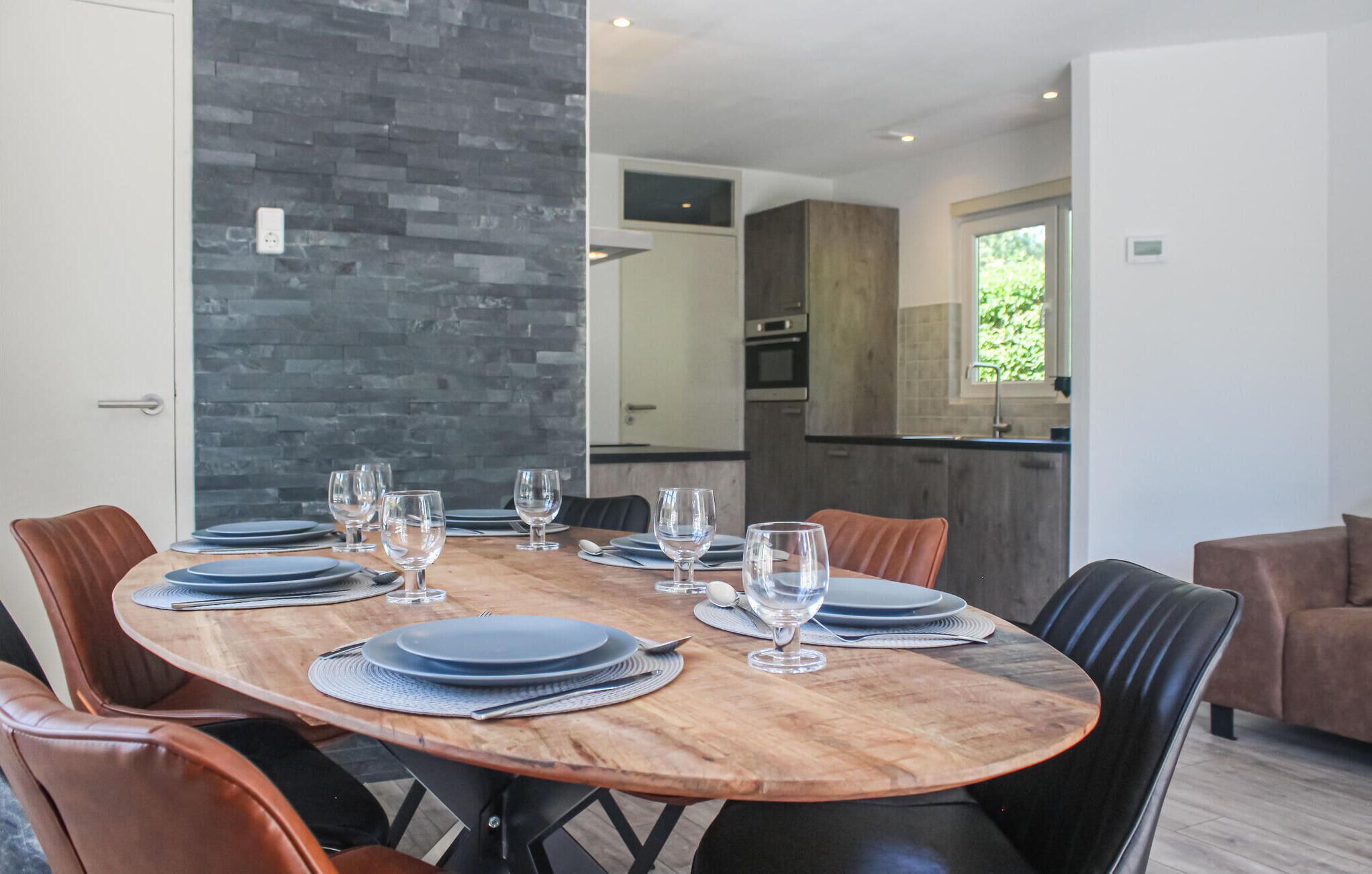 A dining area with a wooden table set for six, surrounded by leather chairs. A kitchen is visible in the background.