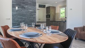 Un comedor con una mesa de madera preparada para seis personas, rodeada de sillas de cuero. Se ve una cocina al fondo.