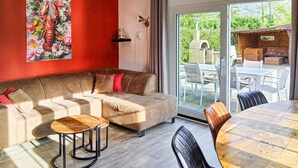 Una sala de estar acogedora con un sofá, una mesa redonda de madera y un ventanal que da a un patio exterior con un horno de ladrillo.