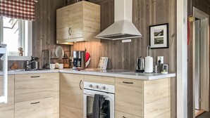 A compact kitchen with wooden cabinets, a built-in oven, a coffee maker, and a hanging light fixture. - Amazing home in Skåbu with sauna (Skåbu)