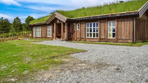 A wooden cabin with a gravel driveway, set on a grassy hill with a clear sky. - Amazing home in Skåbu with sauna (Skåbu)