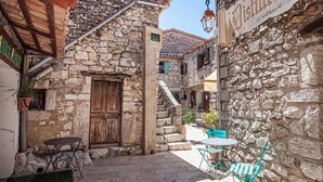 Un estrecho callejón de piedra con una puerta de madera, una mesa pequeña y sillas.