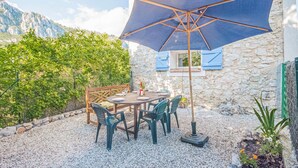 Un patio con una mesa y sillas, una sombrilla azul y un muro de piedra.