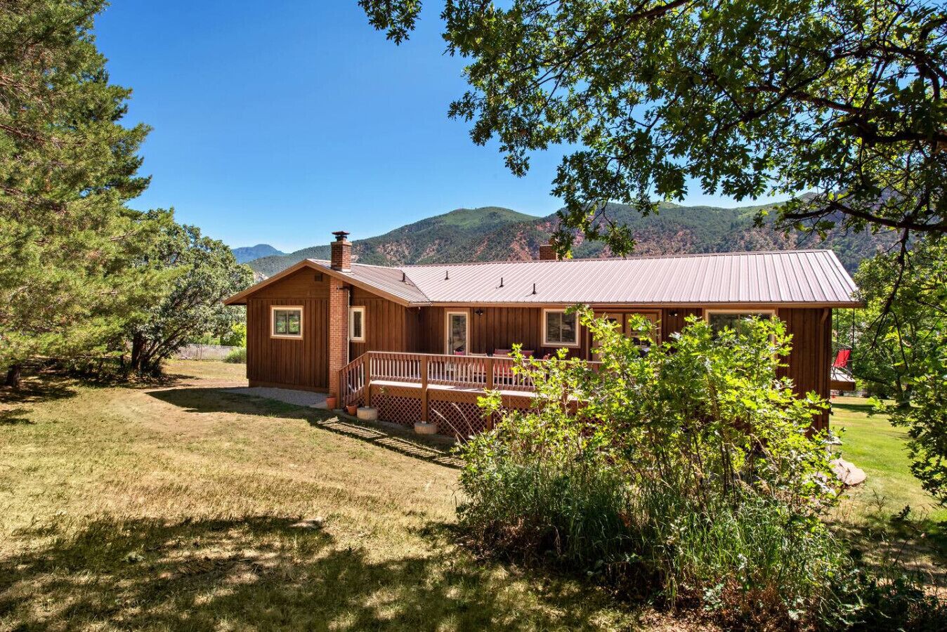 A wooden cabin with a porch, surrounded by trees and mountains.