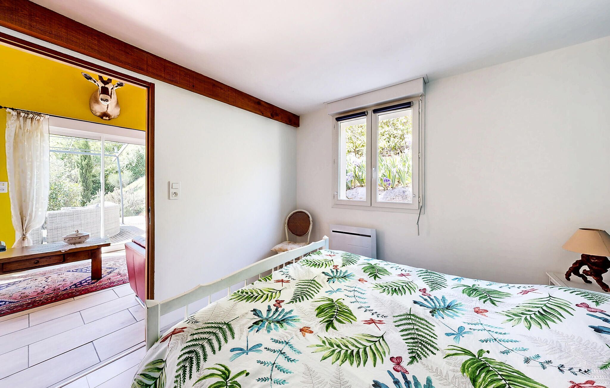 Ein Schlafzimmer mit Bett, Fenster, Stuhl und Tisch mit Pflanze.