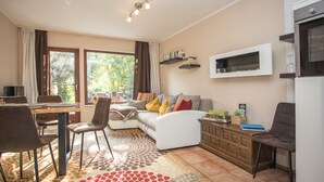 A modern living room with a sofa, chairs, a dining table, and a kitchen area with a microwave. - Vacation cottage in Hildfeld (Winterberg)
