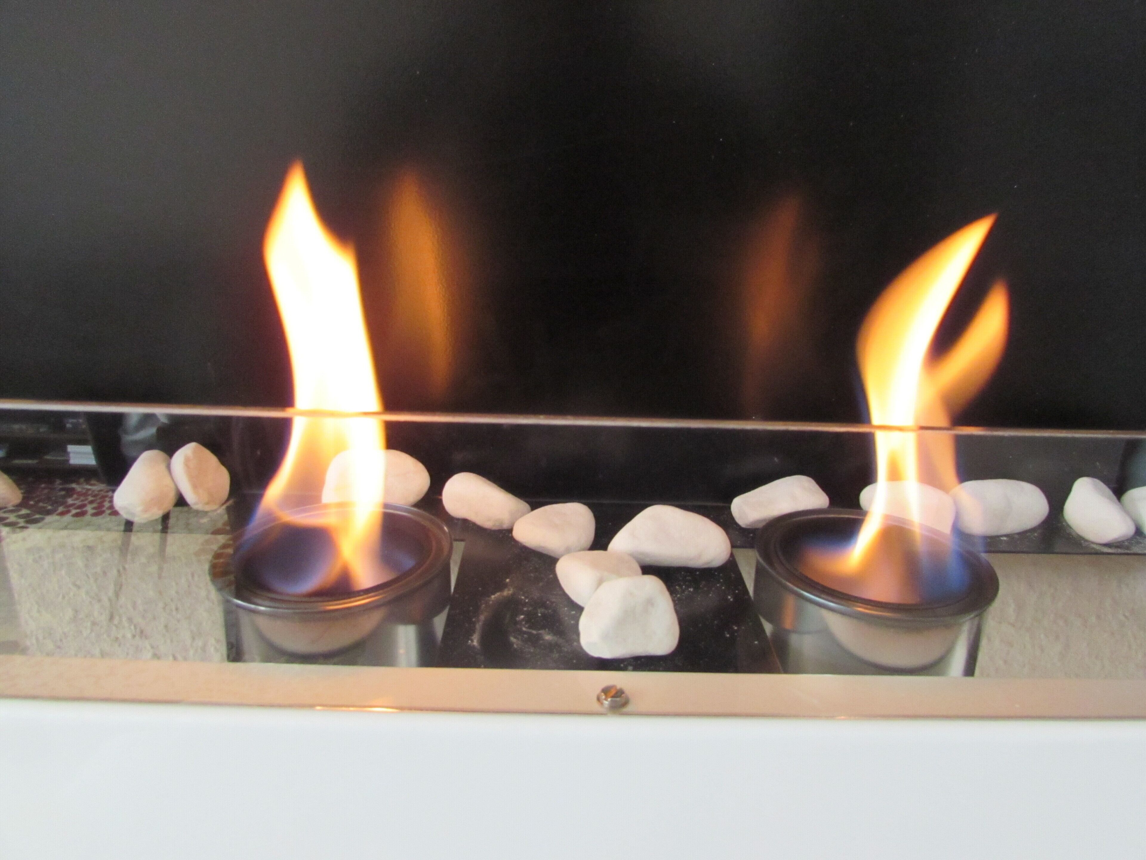 Une cheminée avec deux bougies allumées et des pierres blanches.