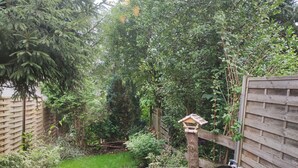 A patio with a table and chairs, surrounded by a wooden fence and lush greenery. - Vacation cottage in Hildfeld (Winterberg)