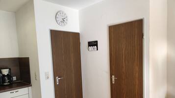 Een hotelkamer met een houten deur, een wandklok, een koffiezetapparaat op een aanrecht, en een bord met een bericht.