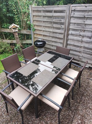 An outdoor patio with a glass-top table and wicker chairs, surrounded by a wooden fence and greenery. - Vacation cottage in Hildfeld (Winterberg)