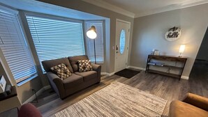 A living room with a sofa, a rug, a lamp, and a door with a 'hello' sign. - Updated, Comfortable and Luxury Stay in our 5 bedroom home.Close to Lagoon,Golf. (Woods Cross)