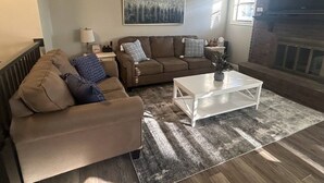 A living room with a brown sofa, a white coffee table, and a fireplace. - Updated, Comfortable and Luxury Stay in our 5 bedroom home.Close to Lagoon,Golf. (Woods Cross)
