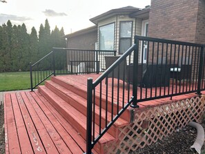 A wooden deck with a black railing leading to a house entrance.