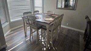 A dining area with a wooden table and chairs, a large window with blinds, and a mirror on the wall. - Updated, Comfortable and Luxury Stay in our 5 bedroom home.Close to Lagoon,Golf. (Woods Cross)