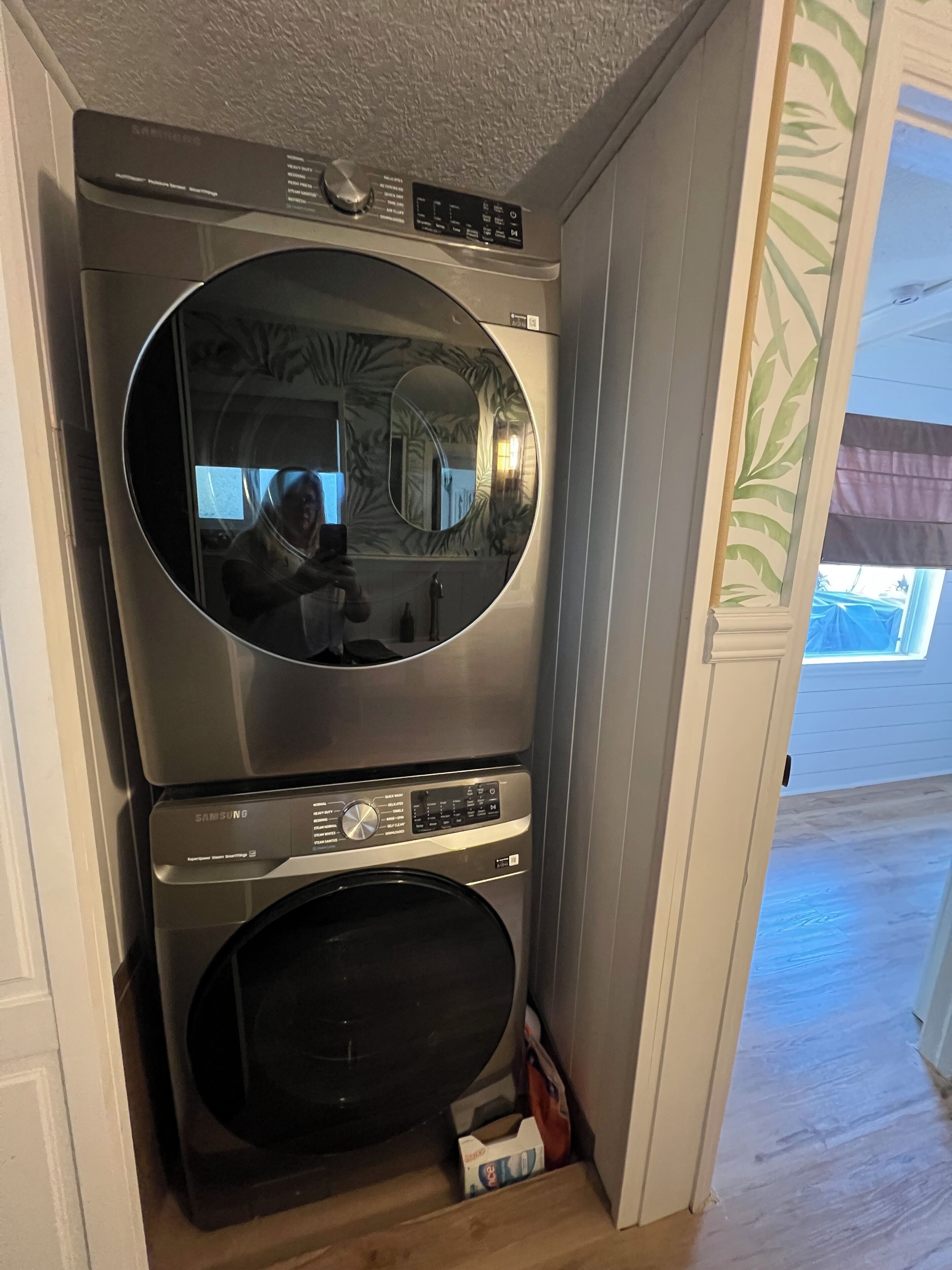 Una unidad compacta de lavadora y secadora con panel de control, un espejo circular y un pequeño espacio de almacenamiento debajo.