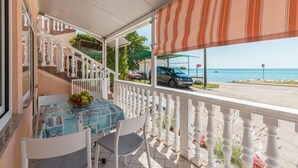 Un balcon avec une table et des chaises, une vue sur la mer et une voiture garée.