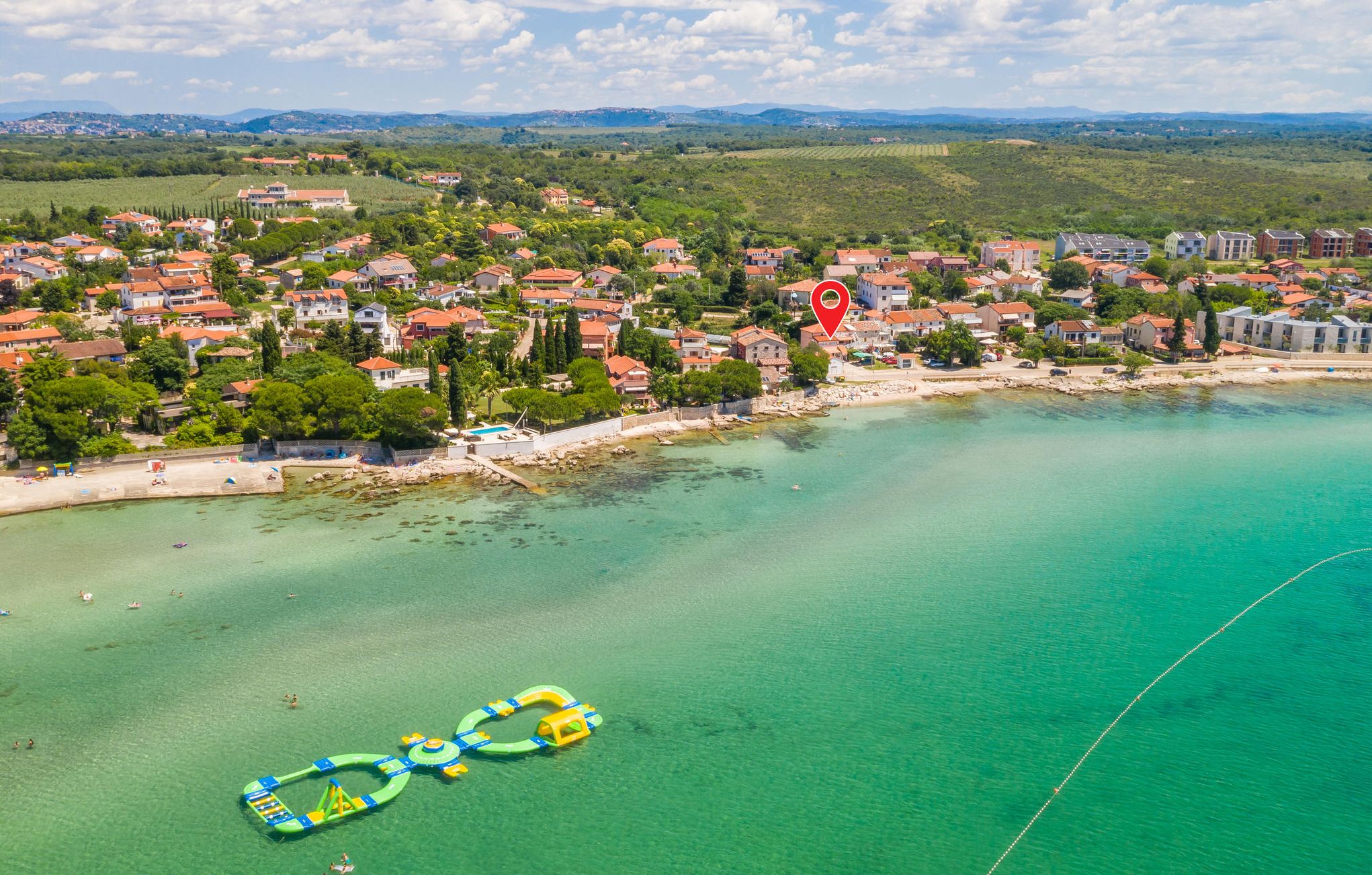 An aerial view of a coastal town with houses, a beach, and clear turquoise waters.