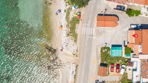 Vue aérienne d’une zone côtière avec une plage, une route et des bâtiments aux toits recouverts de tuiles rouges.
