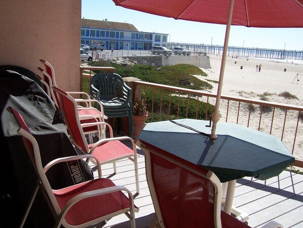 Un balcon avec une table et des chaises donnant sur une plage et une jetée.