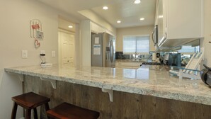A kitchen with granite countertops, wooden bar stools, a stainless steel refrigerator, and a window with blinds. - 110 Pismo Shores: 2  BR, 1.5  BA Condominium in Pismo Beach, Sleeps 6 (Pismo Beach)