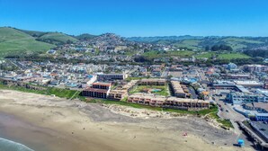 An aerial view of a coastal town with a beach, residential buildings, and a hilly backdrop. - 110 Pismo Shores: 2  BR, 1.5  BA Condominium in Pismo Beach, Sleeps 6 (Pismo Beach)