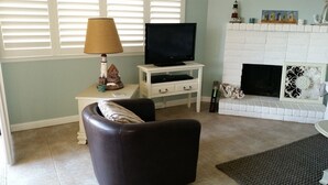 Una sala de estar con televisión sobre un mueble bajo, chimenea y lámpara.