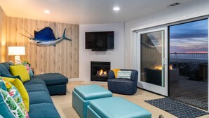 En moderne stue med en modulsofa, en pejs, en ophængt fiskeskulptur og en skydedør, der fører til en udendørs terrasse.