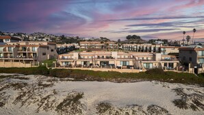 Et kystnært boligområde med moderne lejlighedskomplekser, en sandstrand i forgrunden og en himmel i solnedgang.