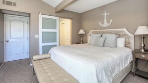 Quarto com uma cama, um banco, uma porta e um objeto decorativo fixado na parede.