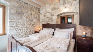A bedroom with a stone wall, wooden beams, a double bed, bedside tables with lamps, and a wooden headboard with floral carvings. - Awesome home in Omis with house a mountain view (Omis)