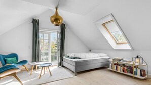 Una camera da letto moderna in stile loft con un lucernario, un letto, una poltrona blu, un tavolino e una libreria.