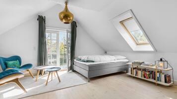 Une chambre de style loft moderne, dotée d’une lucarne, d’un lit, d’une chaise bleue, d’une petite table et d’une bibliothèque.